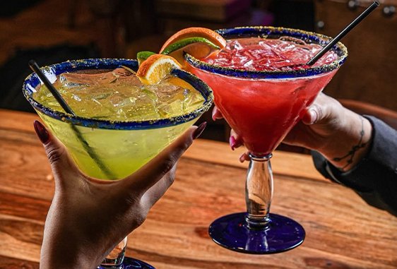 Two margaritas raised in a toast over a wooden table